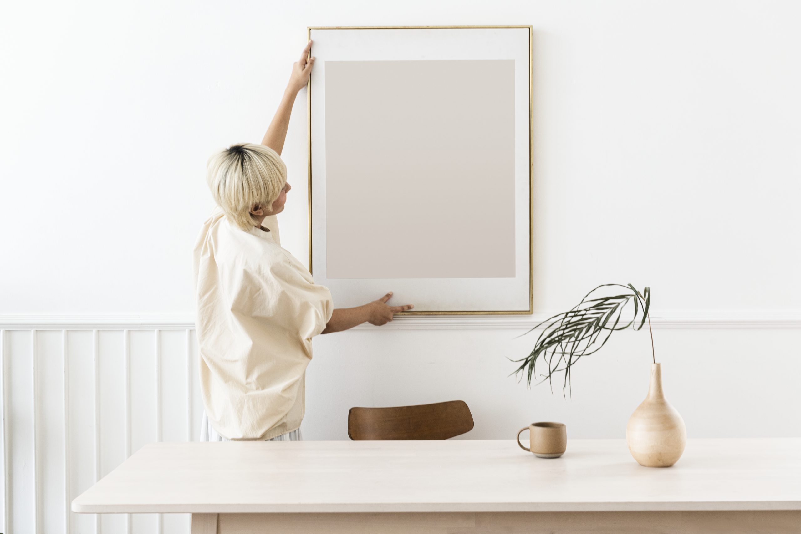 Woman hanging a photo frame on a white wall mockup